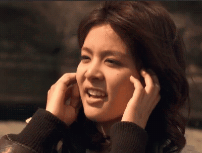 A Woman Is Covering Her Ears With Her Hands And Smiling GIF
