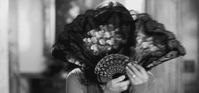 A Woman Is Covering Her Face With A Fan . GIF