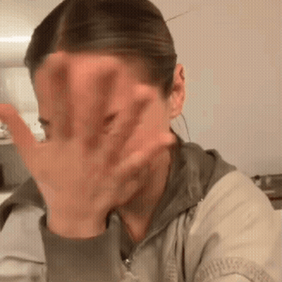 A Woman Is Covering Her Face With Her Hand While Sitting At A Table . GIF