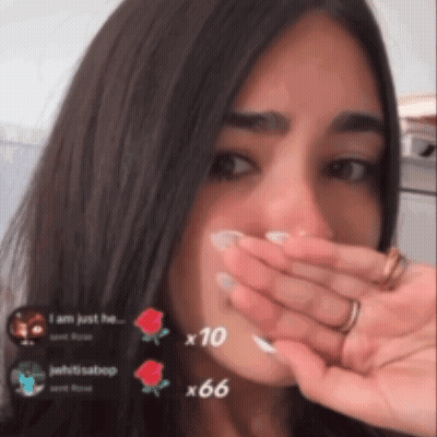 A Woman Is Covering Her Mouth With Her Hand And A Few Roses Are Visible In The Background GIF