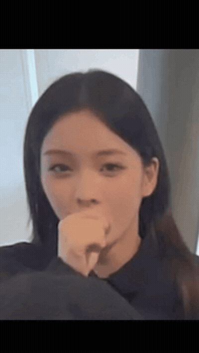 A Woman Is Covering Her Mouth With Her Hand And Looking At The Camera . GIF