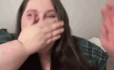 A Woman Is Covering Her Mouth With Her Hand While Laying On A Bed . GIF