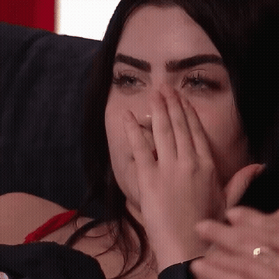 A Woman Is Covering Her Mouth With Her Hand While Sitting On A Couch GIF