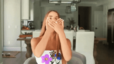 A Woman Is Covering Her Mouth With Her Hands In A Living Room GIF
