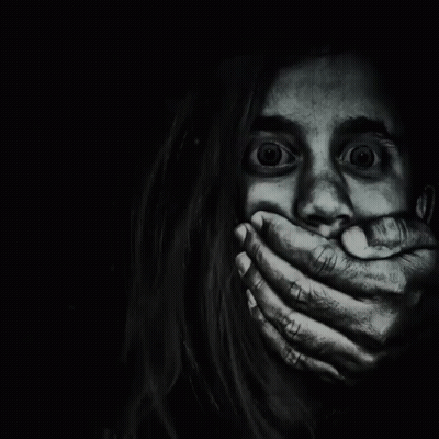 A Woman Is Covering Her Mouth With Her Hands In The Dark GIF