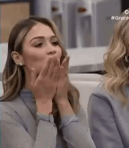 A Woman Is Covering Her Mouth With Her Hands While A Woman Looks On . GIF