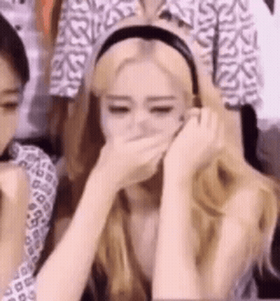 A Woman Is Covering Her Mouth With Her Hands While Sitting In Front Of A Crowd . GIF