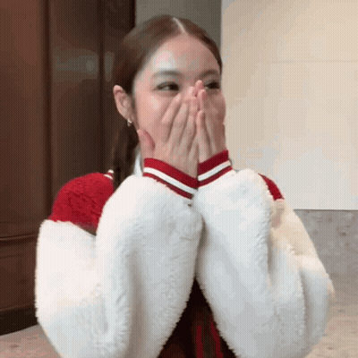 A Woman Is Covering Her Mouth With Her Hands While Wearing A Red And White Jacket . GIF