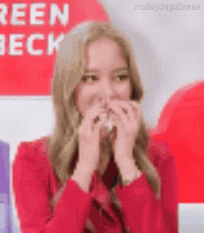 A Woman Is Covering Her Mouth With Her Hands While Wearing A Red Sweater . GIF