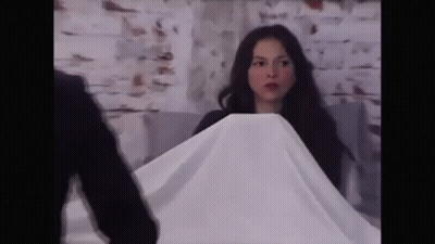 A Woman Is Covering Herself With A White Cloth While A Man Stands Behind Her . GIF