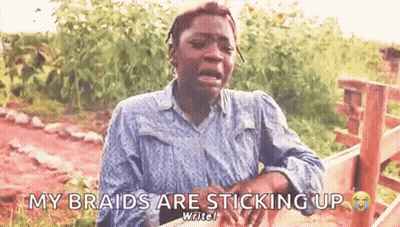 A Woman Is Crying And Saying `` My Braids Are Sticking Up '' While Sitting In Front Of A Wooden Fence . GIF