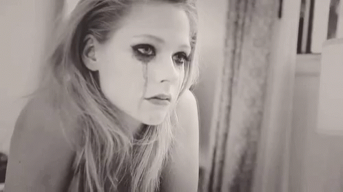 A Woman Is Crying In Front Of A Mirror And Has A Tear Running Down Her Face . GIF