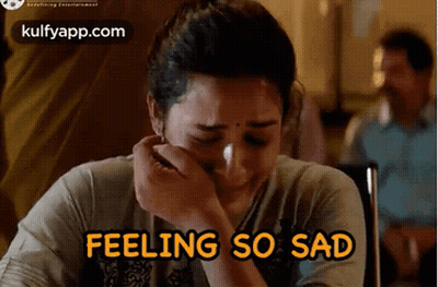 A Woman Is Crying While Sitting At A Table With The Words `` Feeling So Sad '' Written Above Her . GIF