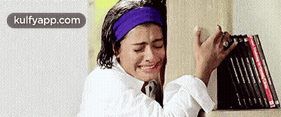 A Woman Is Crying While Standing Next To A Bookshelf . GIF
