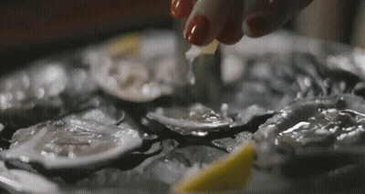 A Woman Is Cutting An Oyster With A Knife On A Plate Of Oysters On Ice . GIF