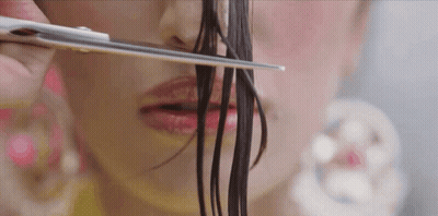 A Woman Is Cutting Her Hair With Scissors In Front Of Her Face GIF
