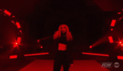 A Woman Is Dancing In A Dark Room With Red Lights . GIF