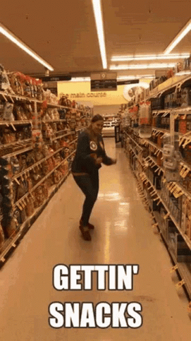 A Woman Is Dancing In A Grocery Store Aisle With The Words Gettin ' Snacks Written On It . GIF