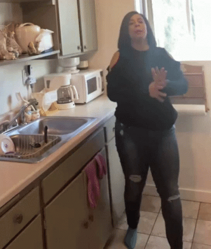 A Woman Is Dancing In A Kitchen In Front Of A Microwave GIF