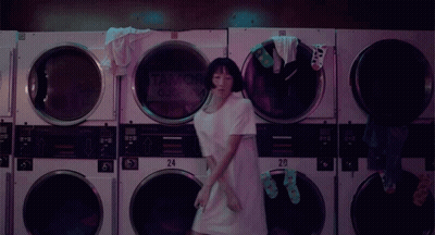 A Woman Is Dancing In A Laundromat With A Sign That Says Tank Queen On It GIF