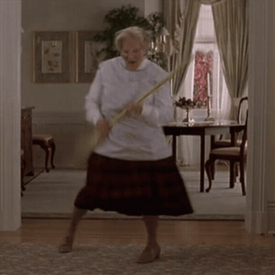 A Woman Is Dancing In A Living Room While Holding A Broom In Her Hand . GIF