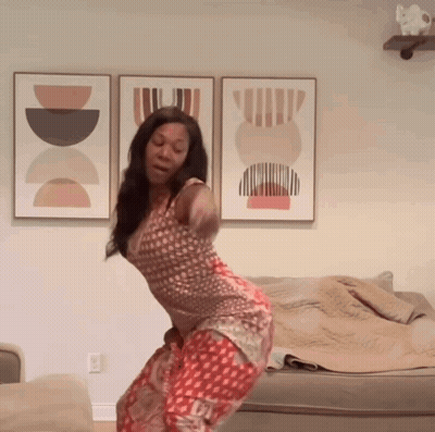 A Woman Is Dancing In A Living Room With A Couch And Paintings On The Wall GIF