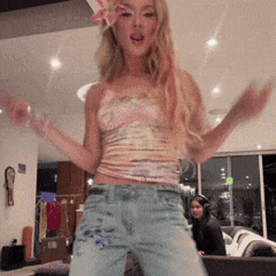 A Woman Is Dancing In A Living Room With A Flower In Her Hair GIF