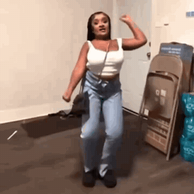 A Woman Is Dancing In A Room In Front Of Folding Chairs . GIF