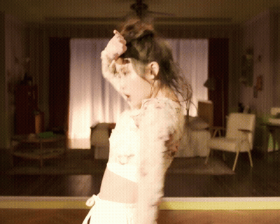 A Woman Is Dancing In A Room With A Ceiling Fan GIF
