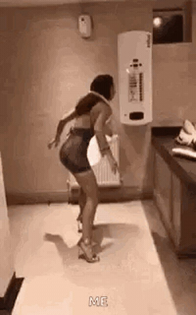 A Woman Is Dancing In A Room With A White Wall And A Heater . GIF