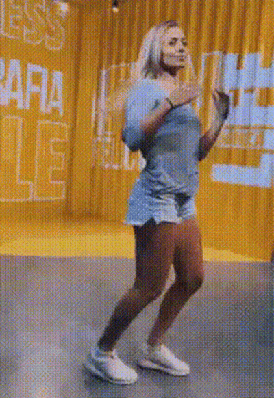 A Woman Is Dancing In A Room With A Yellow Curtain And A Sign That Says ' Ara ' On It . GIF