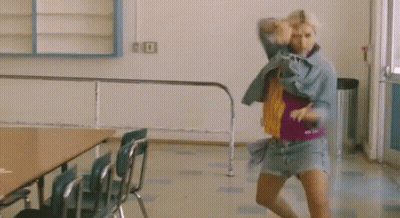 A Woman Is Dancing In A Room With Chairs And A Table . GIF
