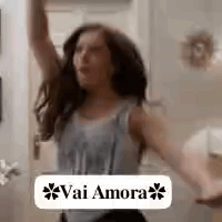 A Woman Is Dancing In A Room With Her Arms In The Air And A Sign That Says Vai Amora . GIF
