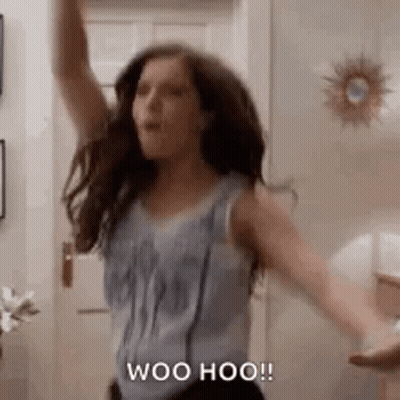 A Woman Is Dancing In A Room With Her Arms In The Air And Saying Woo Hoo . GIF