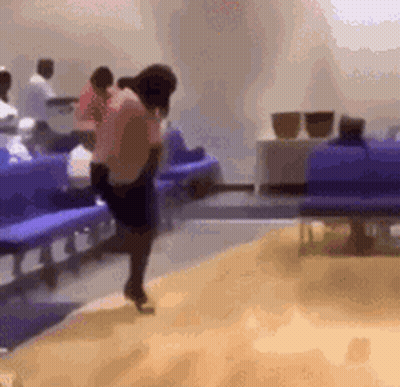 A Woman Is Dancing In A Waiting Room With People Sitting In Blue Chairs . GIF