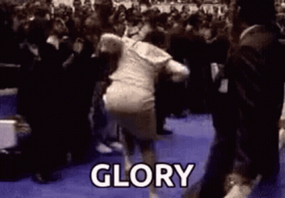 A Woman Is Dancing In Front Of A Crowd And The Word Glory Is Written On The Floor . GIF