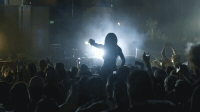 A Woman Is Dancing In Front Of A Crowd At A Concert With A Green Exit Sign In The Background GIF