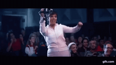 A Woman Is Dancing In Front Of A Crowd Of People In A Theater While Holding A Microphone . GIF