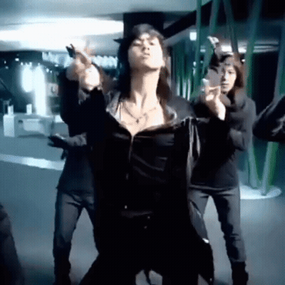 A Woman Is Dancing In Front Of A Group Of People In A Dark Room . GIF