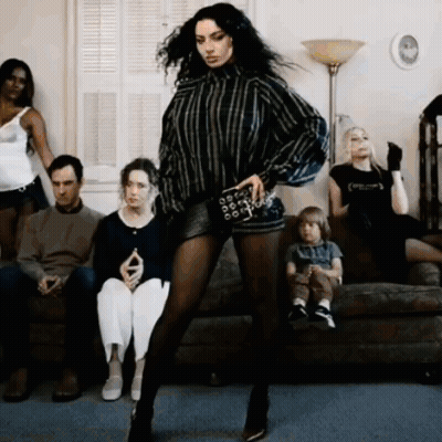 A Woman Is Dancing In Front Of A Group Of People Who Are Sitting On A Couch GIF