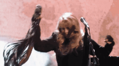 A Woman Is Dancing In Front Of A Microphone While Her Hair Blows In The Wind . GIF