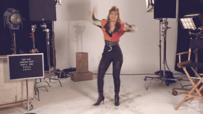 A Woman Is Dancing In Front Of A Sign That Says " Top Gun Screen Test " GIF