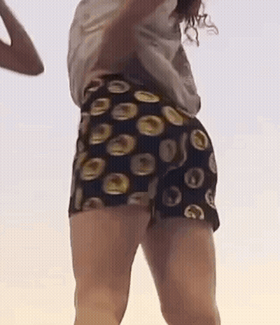 A Woman Is Dancing On A Beach Wearing Shorts With Circles On Them . GIF