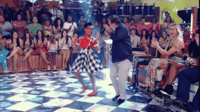 A Woman Is Dancing On A Checkered Floor In Front Of A Crowd Of People . GIF
