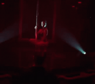 A Woman Is Dancing On A Pole In A Dark Room GIF