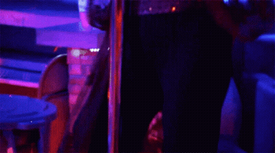 A Woman Is Dancing On A Pole In A Dark Room With Glow In The Dark Bracelets On Her Wrists . GIF