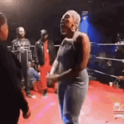 A Woman Is Dancing On A Red Carpet In A Boxing Ring While A Man Talks To Her . GIF