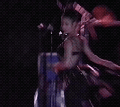 A Woman Is Dancing On A Stage In Front Of A Microphone In A Dark Room . GIF