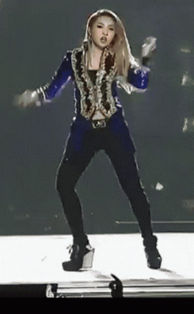 A Woman Is Dancing On A Stage Wearing A Blue Jacket And Black Pants GIF