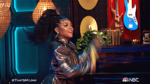 A Woman Is Dancing On A Stage With A Guitar In The Background GIF